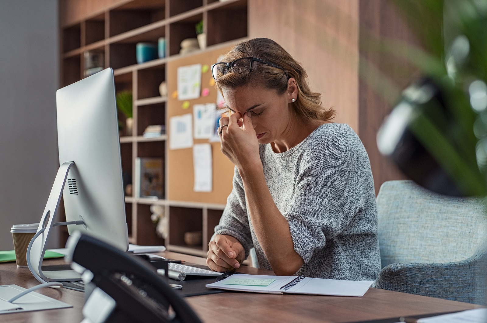 Exhausted businesswoman having a headache at office. Mature creative woman working at office desk feeling tired. Stressed casual business woman feeling eye pain while overworking on desktop computer.