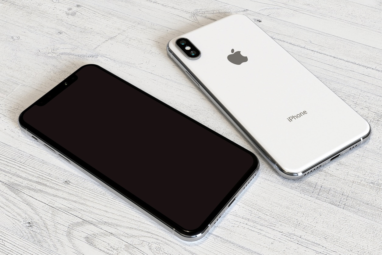 Apple iPhone XS Silver smartphone, comparison of the front side (screen) and the back side (camera) side by side, on a white wood surface. White OLED screen.
Commercial editorial image, high angle perspective.