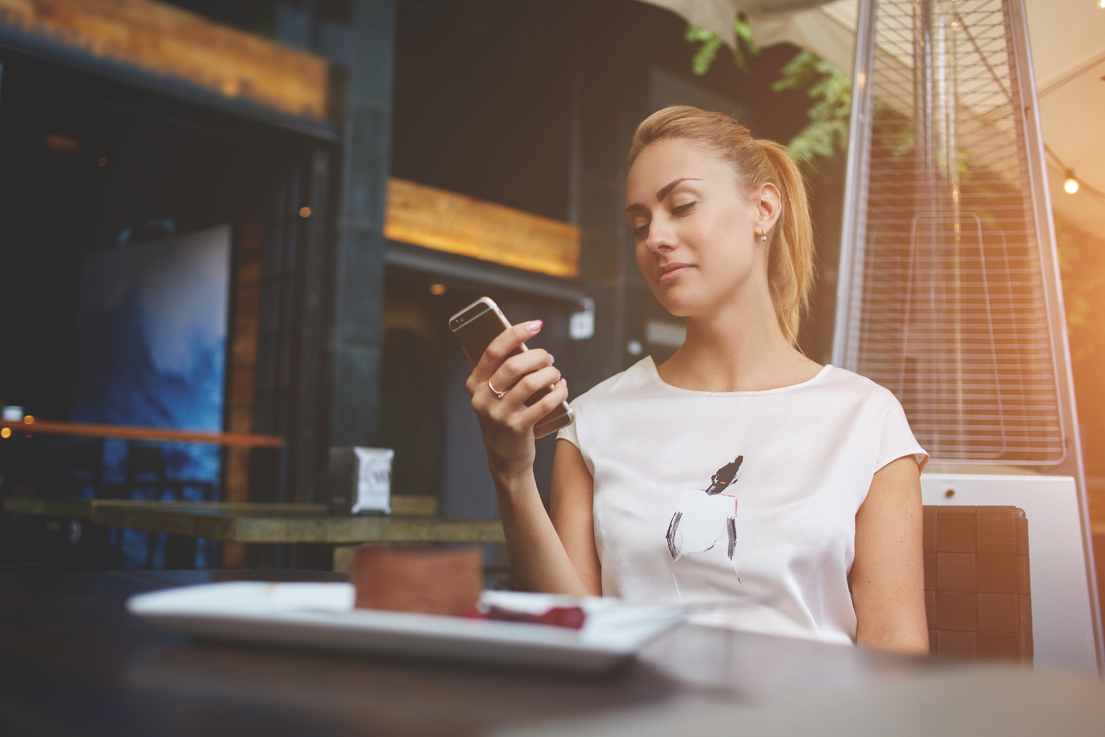 Charming European female browsing wifi via mobile phone during morning breakfast in cafe bar beautiful woman reading text message on her cell telephone while sitting in coffee shop during free time