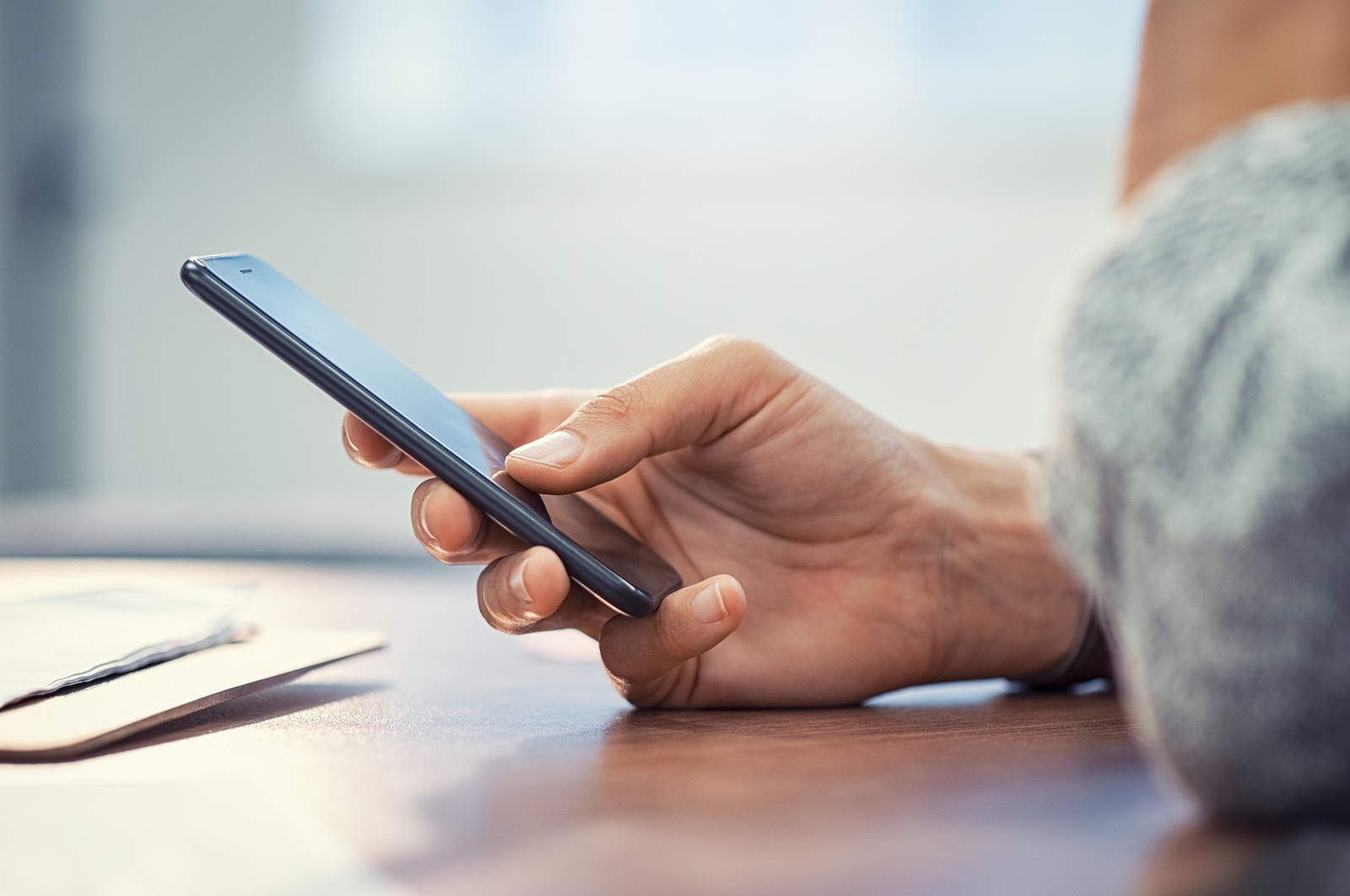 Closeup hand of woman using smartphone on wooden table. Businesswoman typing text message on smart phone. Casual lady hand holding mobile phone with blank screen at office.