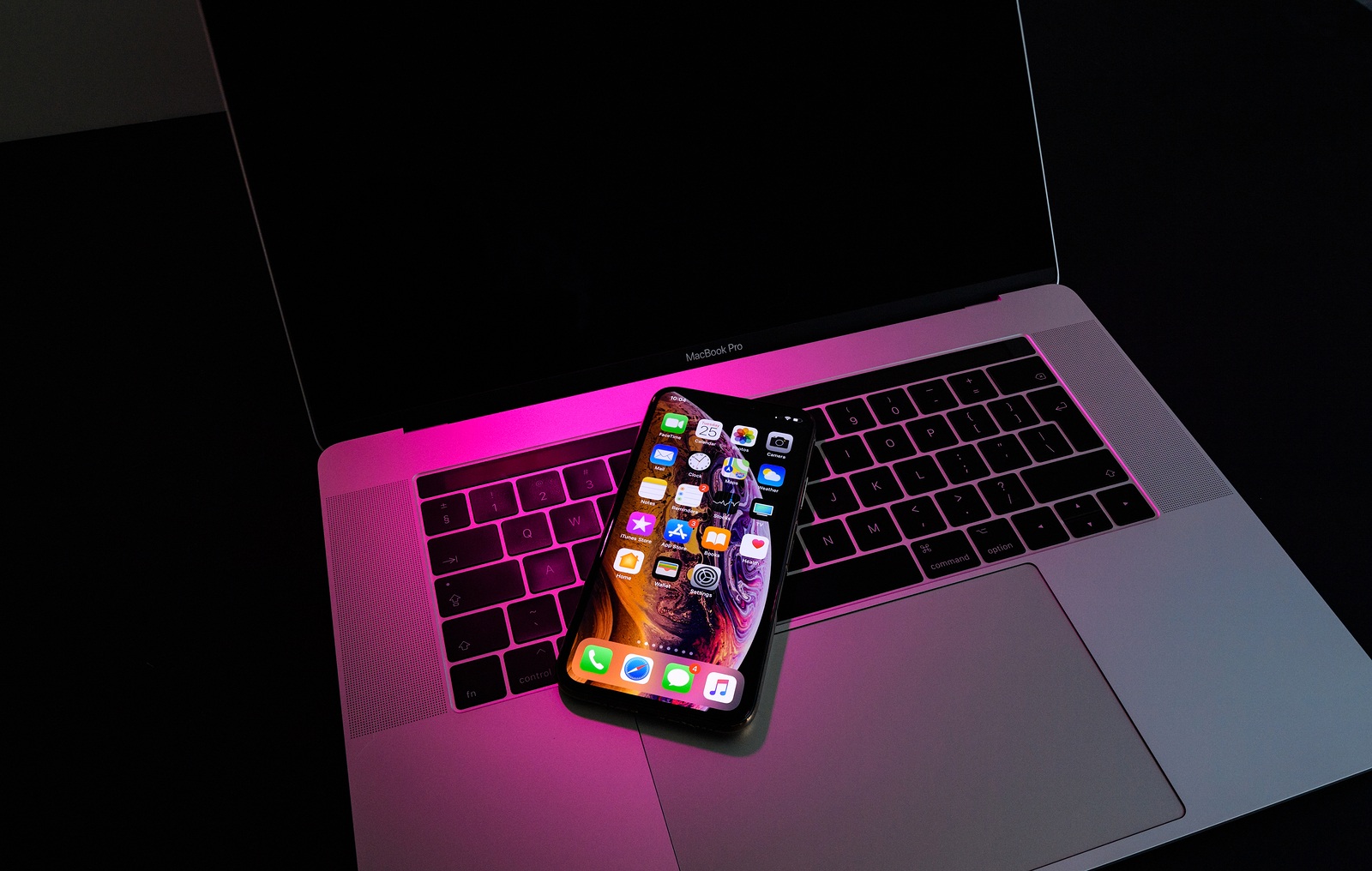 PARIS, FRANCE - SEP 25, 2018: New iPhone Xs and Xs Max smartphone model by Apple Computers close up. Newest golden Apple Iphone on pink magenta light on Macbook Pro 15 laptopkeyboard