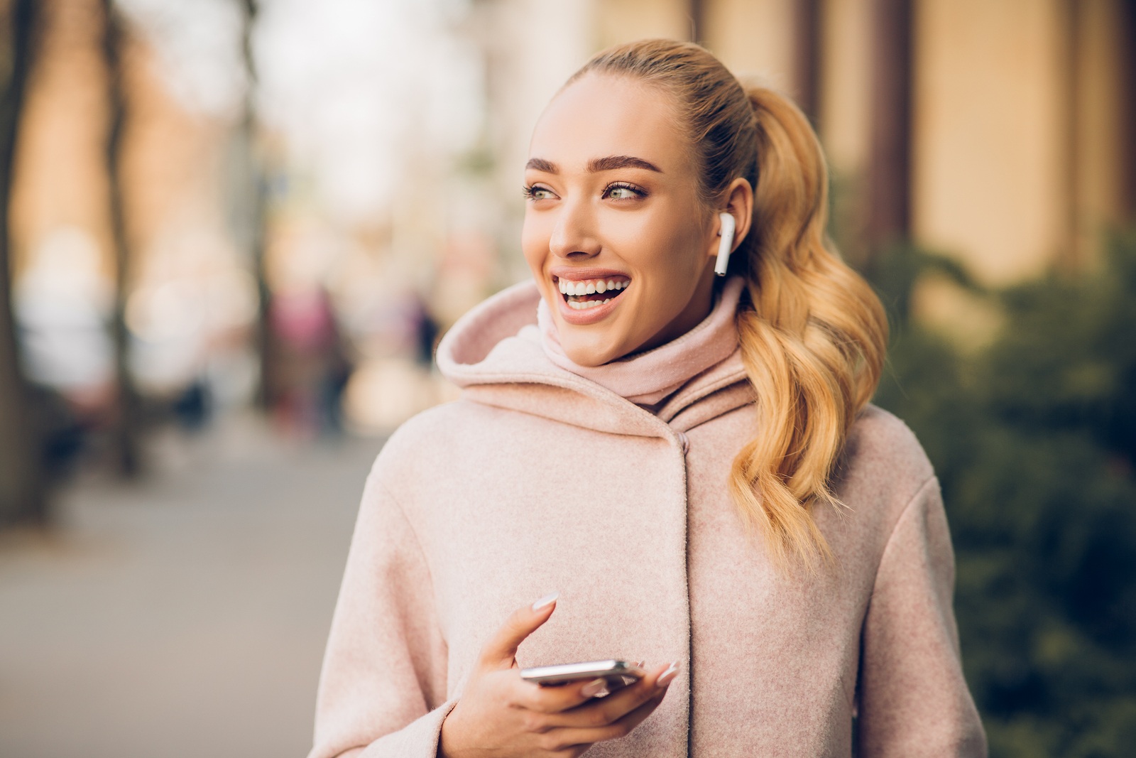 Stylish woman listening music on her airpods, walking in city at autumn day