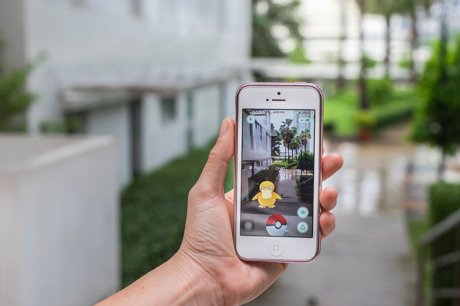 Bangkok, Thailand - Aug 7, 2016 : Hand holding Apple iphone5 mobile phone showing the Pokemon Go application at screen over the walk way with park photo blurred background on August 7, 2016, thailand