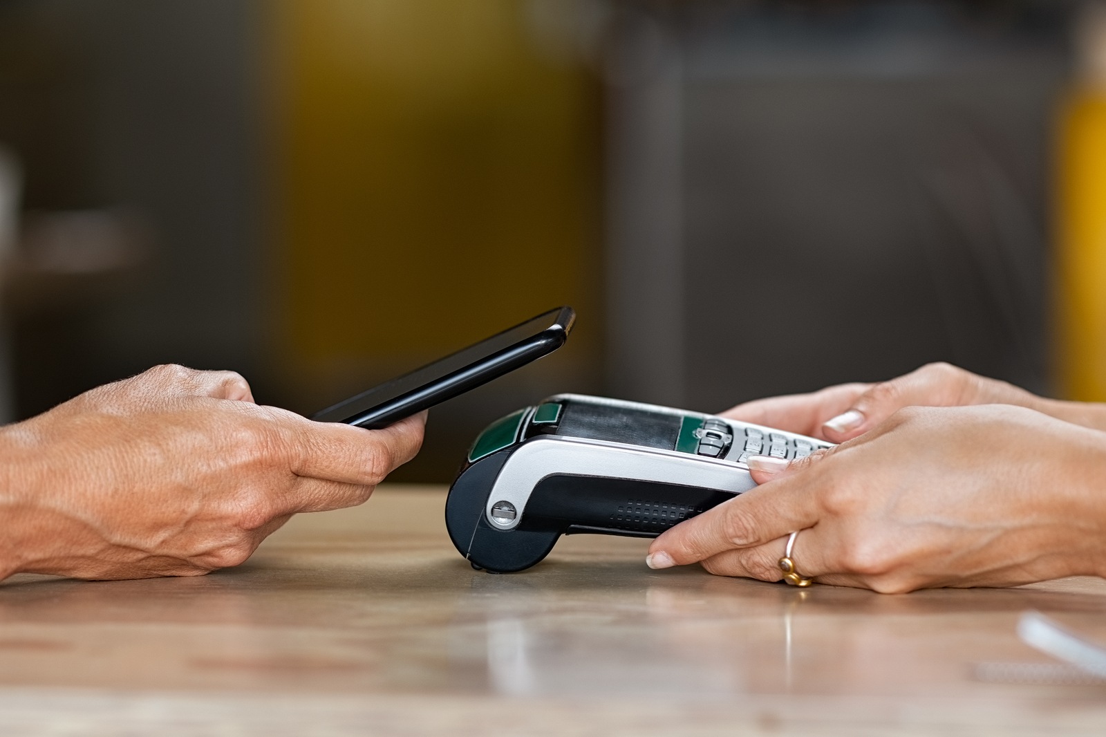 Closeup of woman hand paying a bill through smartphone using NFC technology. Closeup of hand holding pos terminal to receive payment using phone. Customer using mobile to make payment with contactless