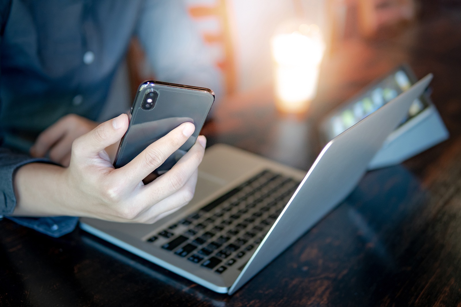 Male hand holding smartphone. Businessman using laptop computer and digital tablet while working in the cafe. Mobile app or internet of things concepts. Modern lifestyle in digital age.