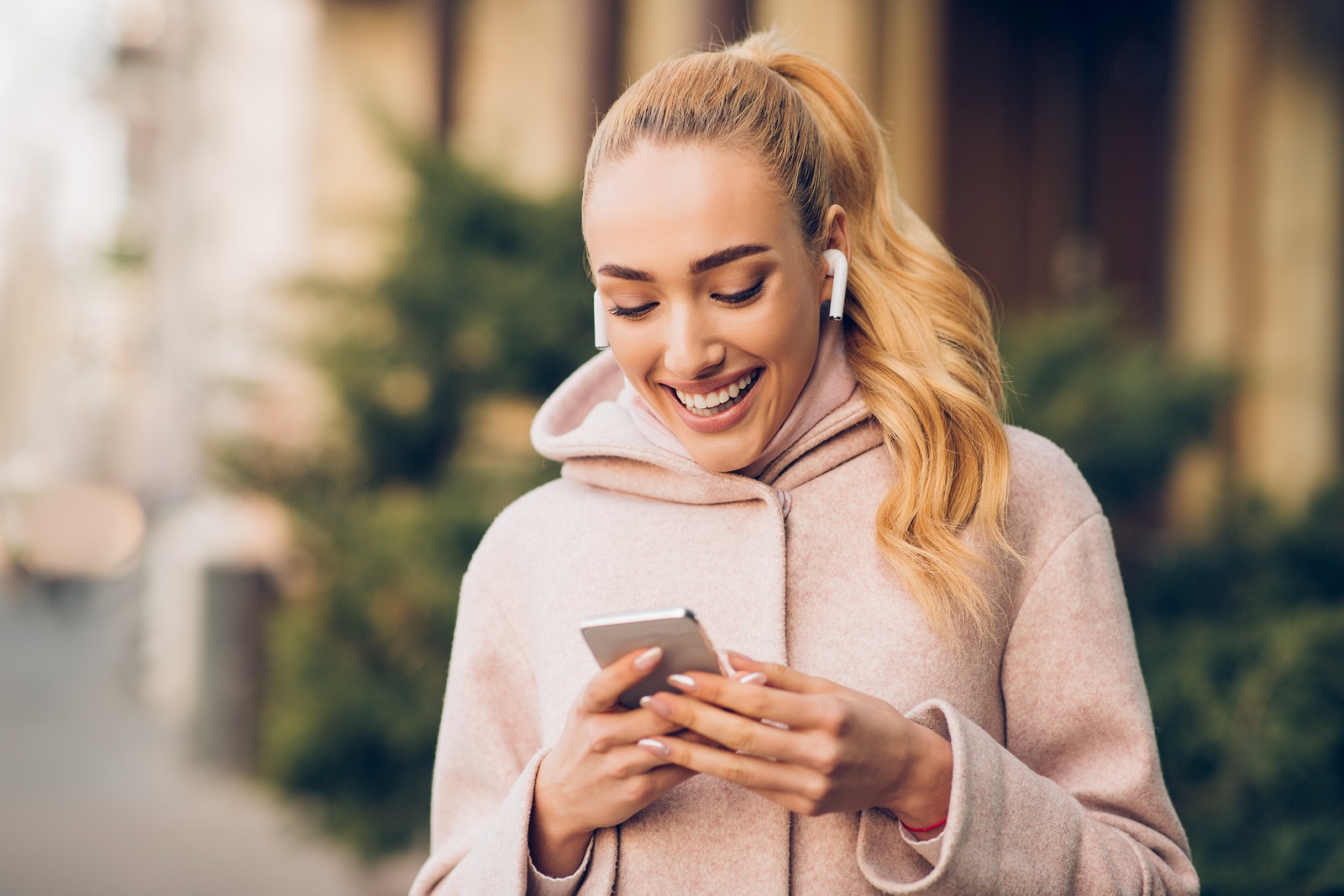 Woman messaging on phone outdoors on city street, listening music in airpods