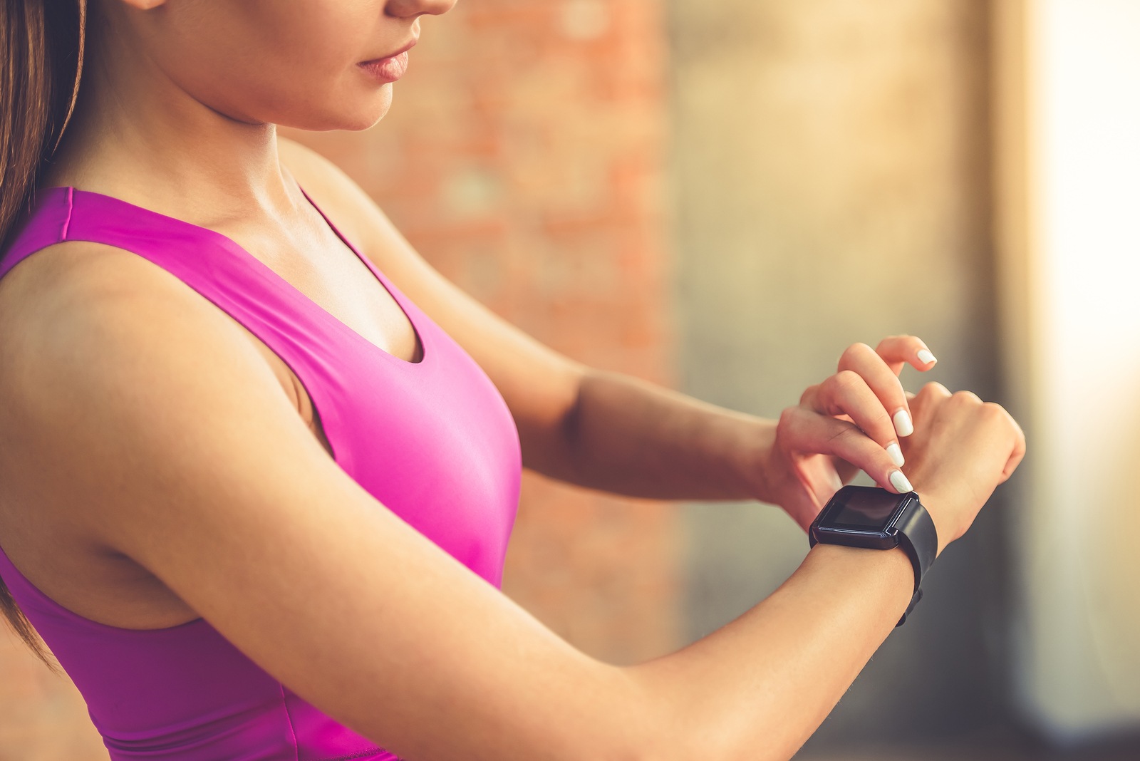 Cropped image of beautiful sports girl is switching on her fitbit before training while standing in fitness hall