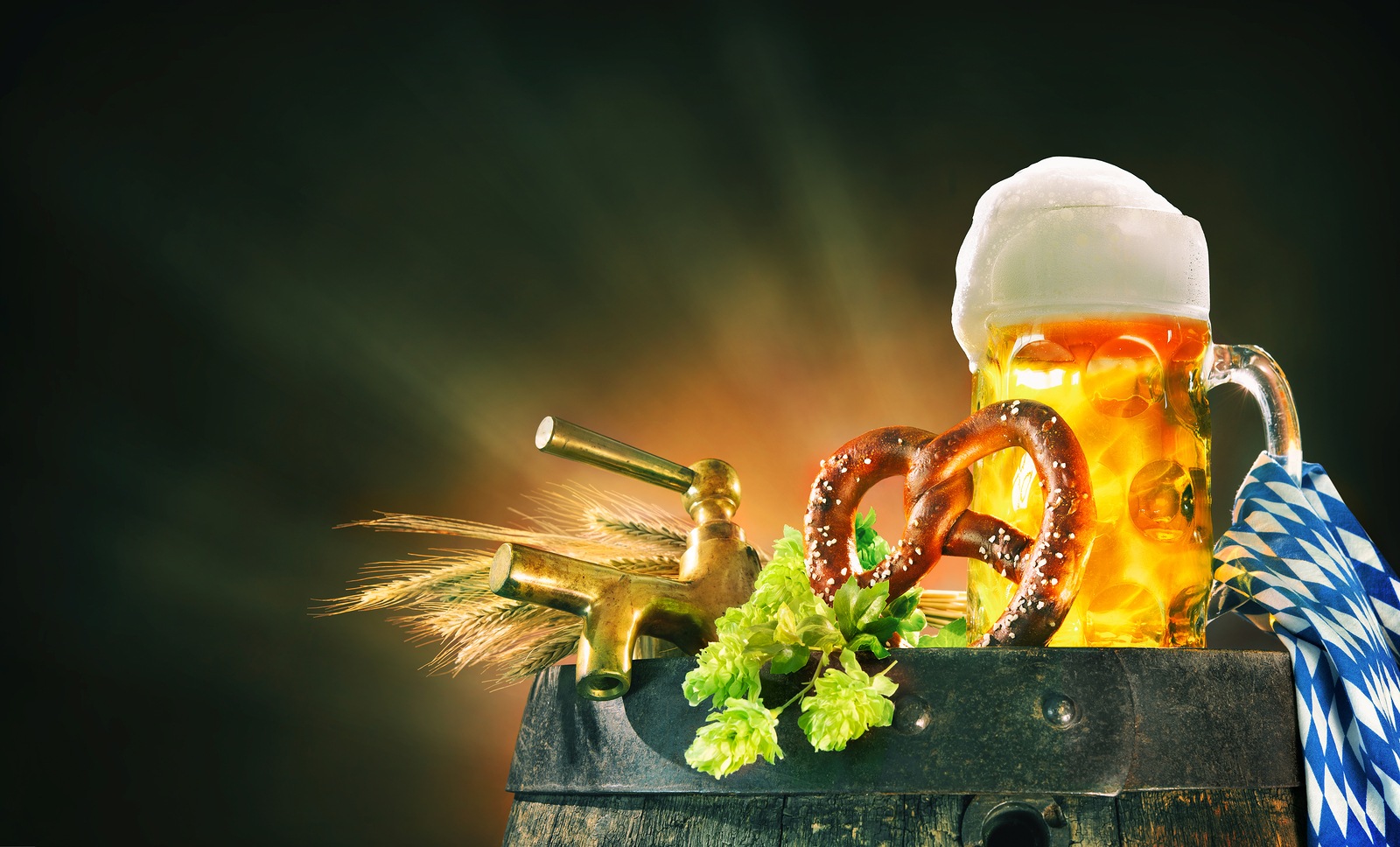 Oktoberfest background with beer stein, beer tap, pretzel, wheat and hops on a barrel