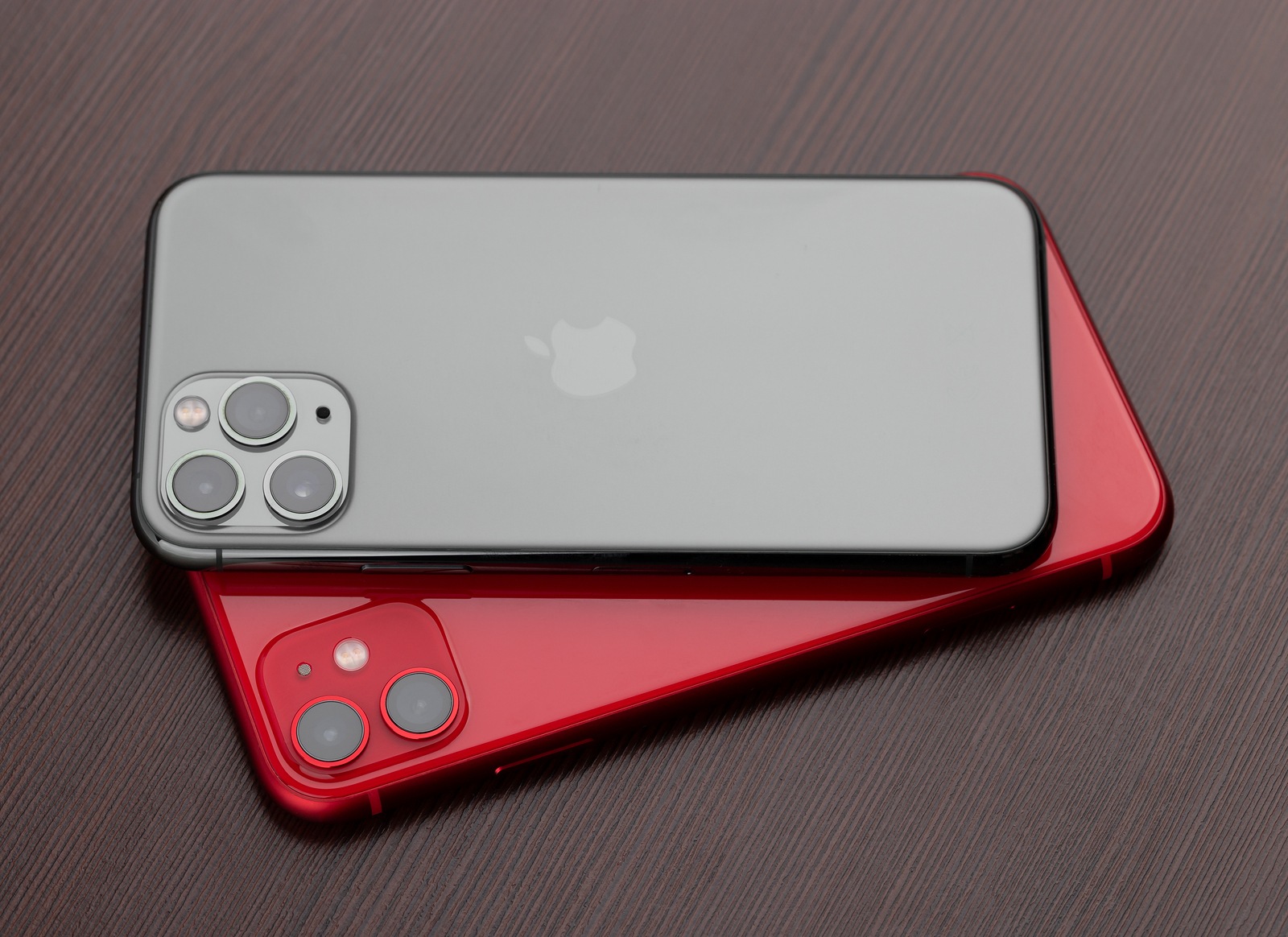 Rostov-on-Don, Russia - November 2019. Apple iPhone 11 PRODUCT RED and Apple iPhone 11 Pro Midnight Green on a wooden surface. Two smartphones from Apple company close-up.