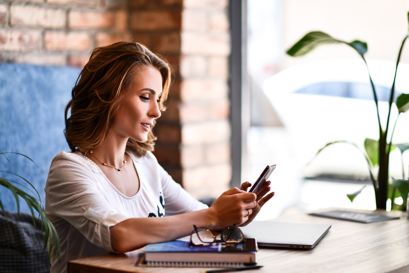 Charming woman with beautiful smile reading good news on mobile phone during rest in coffee shop, happy Caucasian female watching her photos on cell telephone while relaxing in cafe during free time