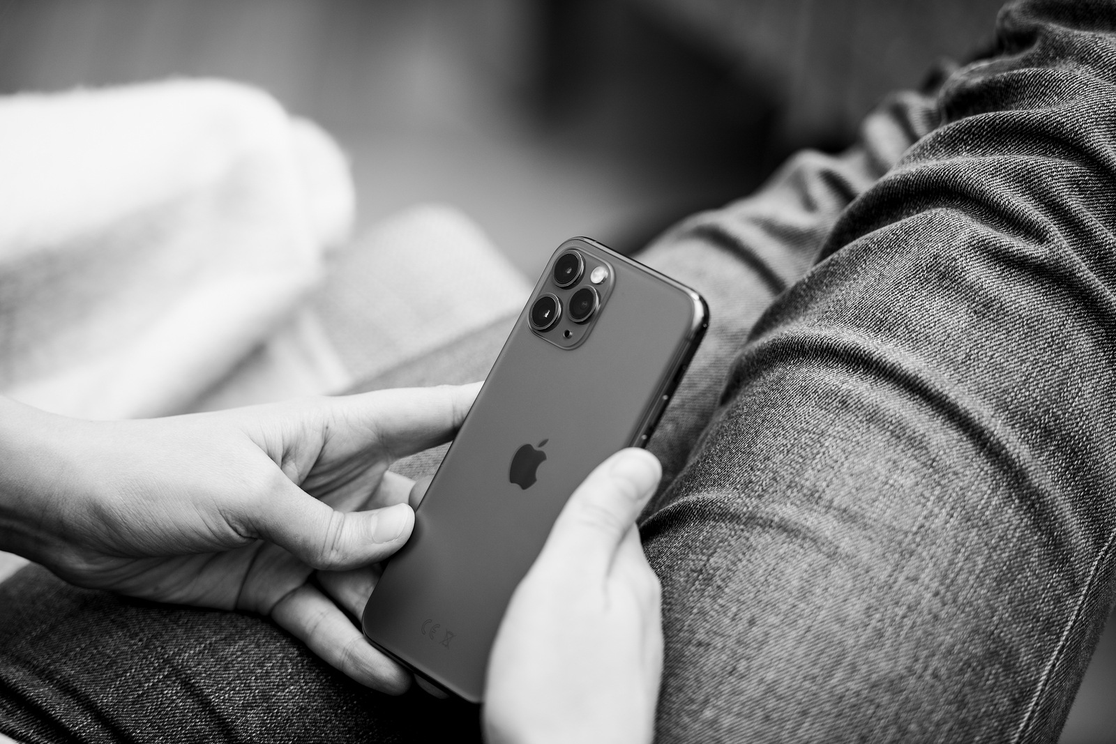 Paris, France - Sep 27, 2019: Black and white image of Elegant young woman looking at matte glass of latest Apple Computers iPhone 11 Pro with triple-camera using smartphone in business living room sofa