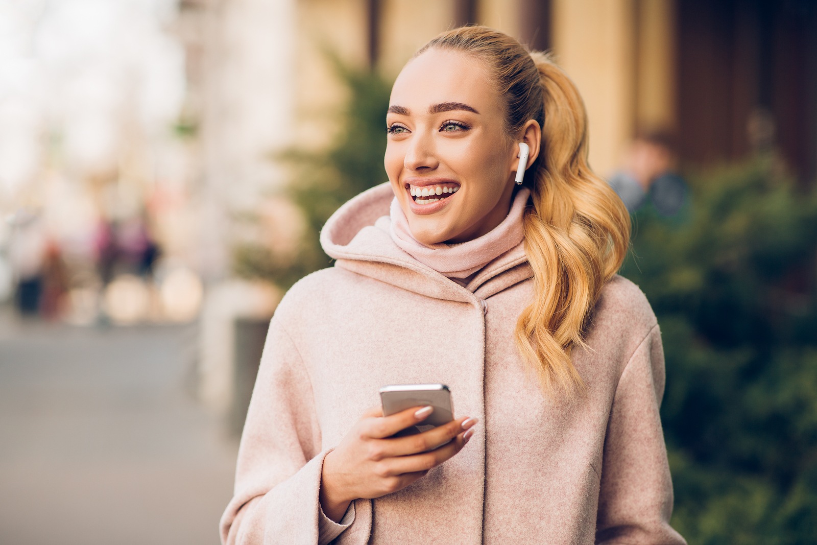 Happy woman walking in city and listening music in airpods, enjoying weekend