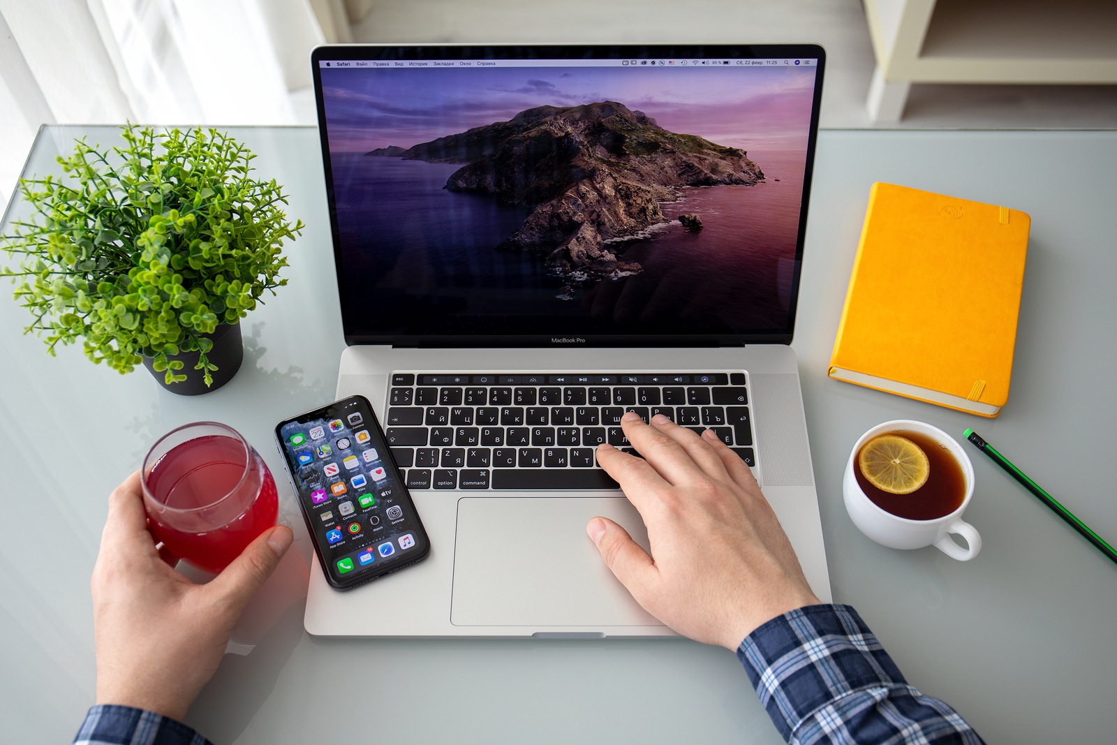 Anapa, Russia - February 22, 2020: Backgrounds MacOS Catalina on screen MacBook Pro 16 and iPhone 11 in the table man hand. MacBook Pro 16 and iPhone 11 was created and developed by the Apple inc.