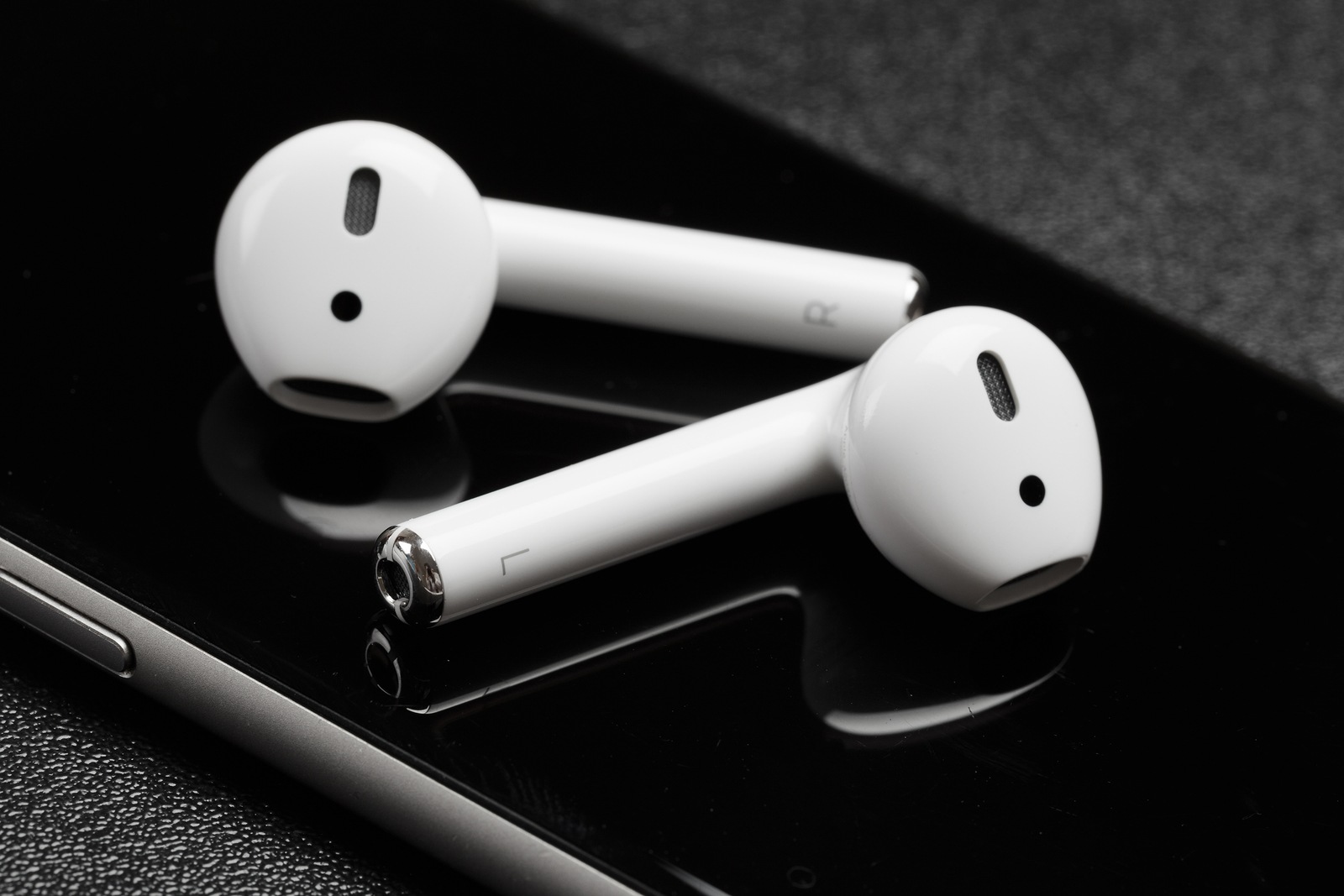 white Apple AirPods lie on a dark black surface of iPhone