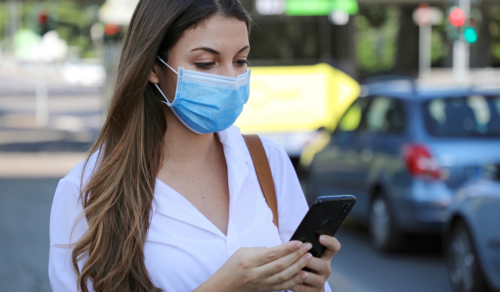 COVID-19 Pandemic Coronavirus Mobile Application - Young Woman Wearing Surgical Mask Using Smart Phone App in City Street to Aid Contact Tracing in Response to the 2019-20 Coronavirus Pandemic