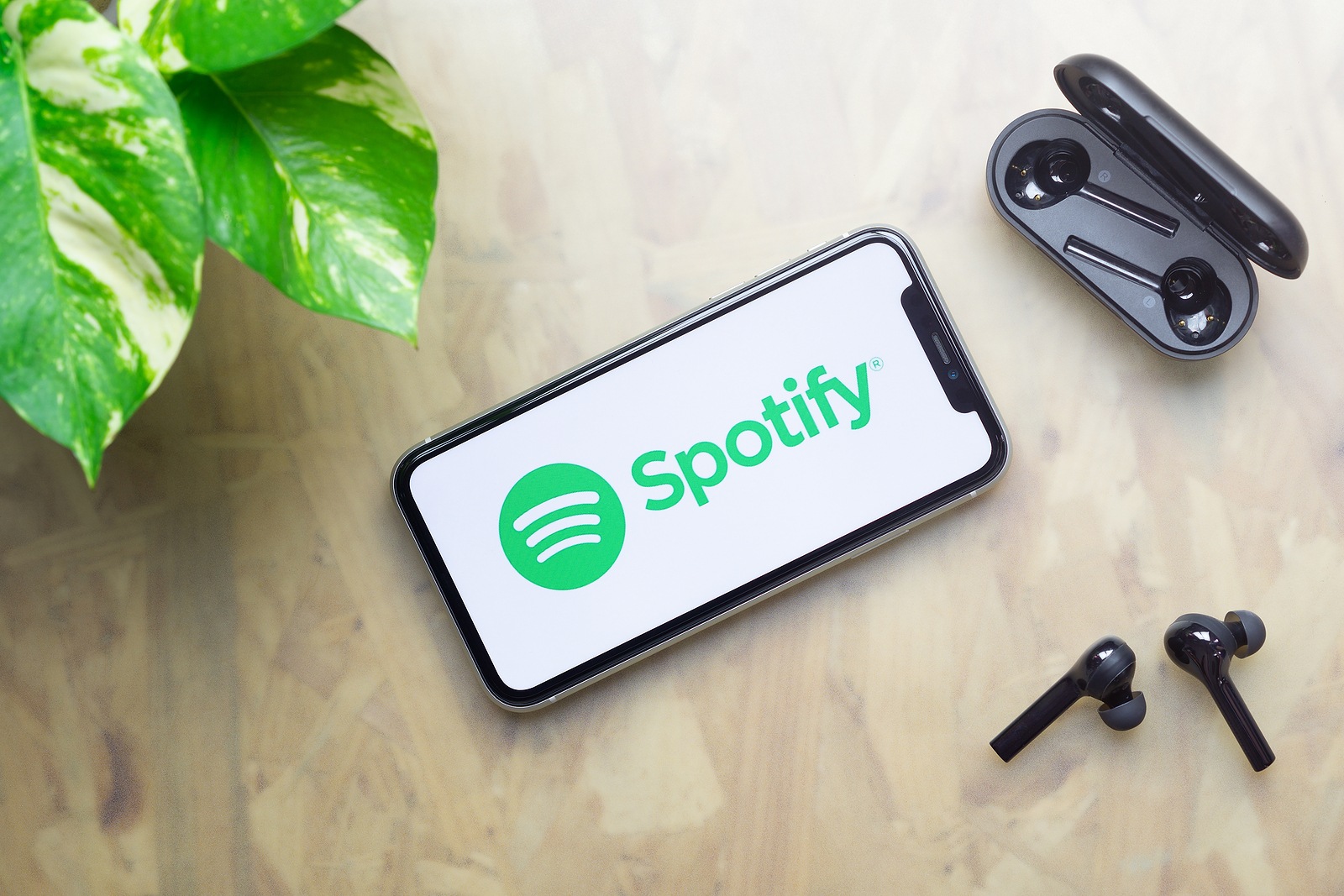 Bangkok, Thailand - July 3, 2020: Apple Iphone 11  with Spotify logo on display, bluetooth headphones with case, green plant on working table background. Flat lay Top view