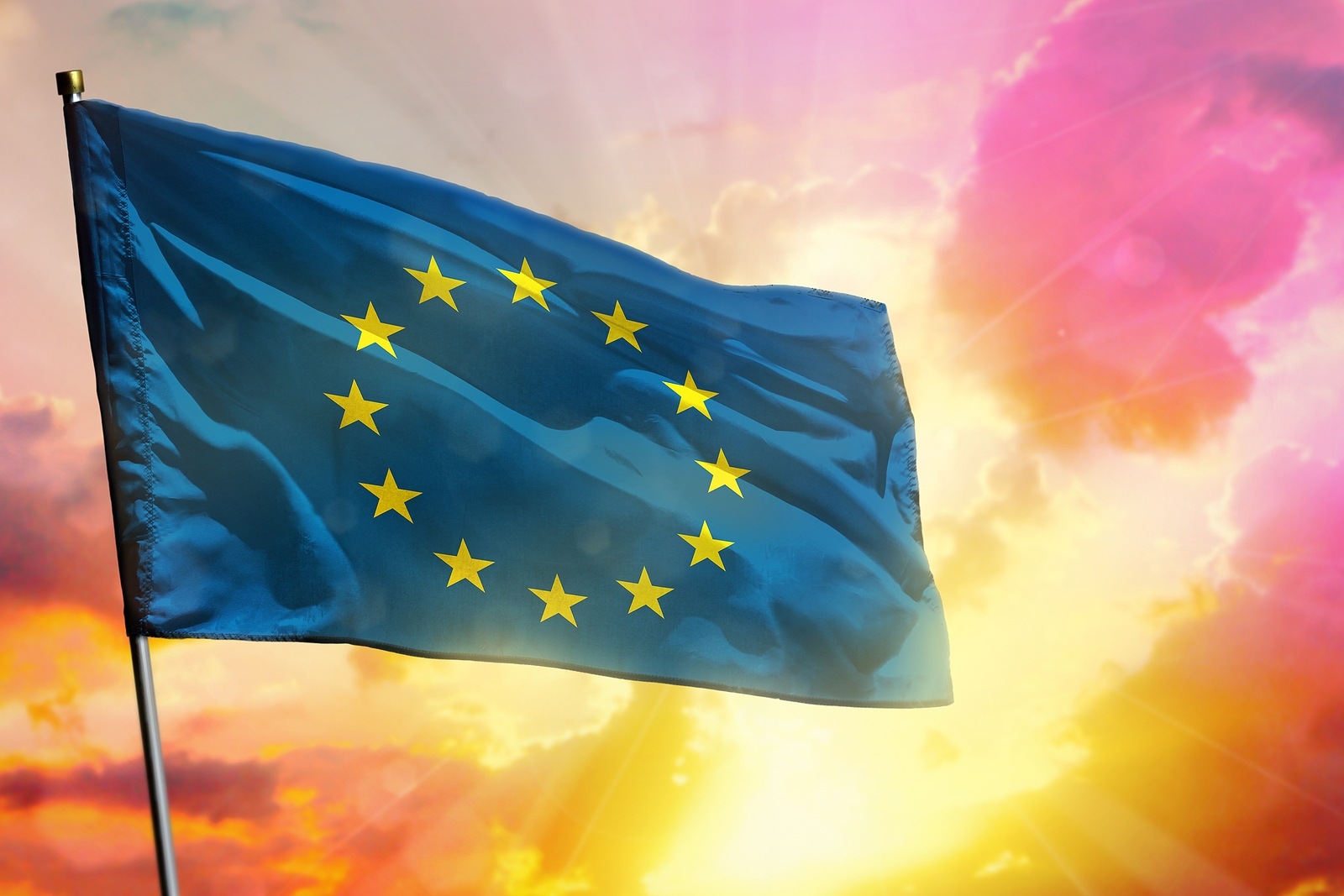 Fluttering European Union flag on beautiful colorful sunset or sunrise background. European Union success and happiness concept.