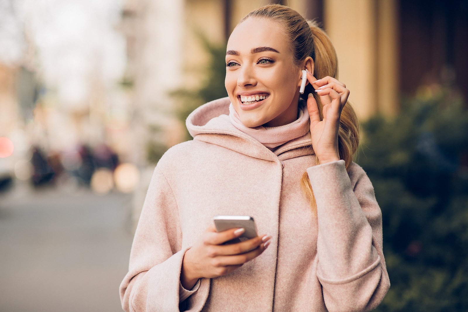 Millennial woman enjoying music in airpods, walking in city on weekend