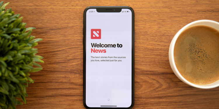 Anapa, Russia - October 13, 2018: iPhone X with news applications on the screen and background wooden desk. iPhone is created and developed by the Apple inc.